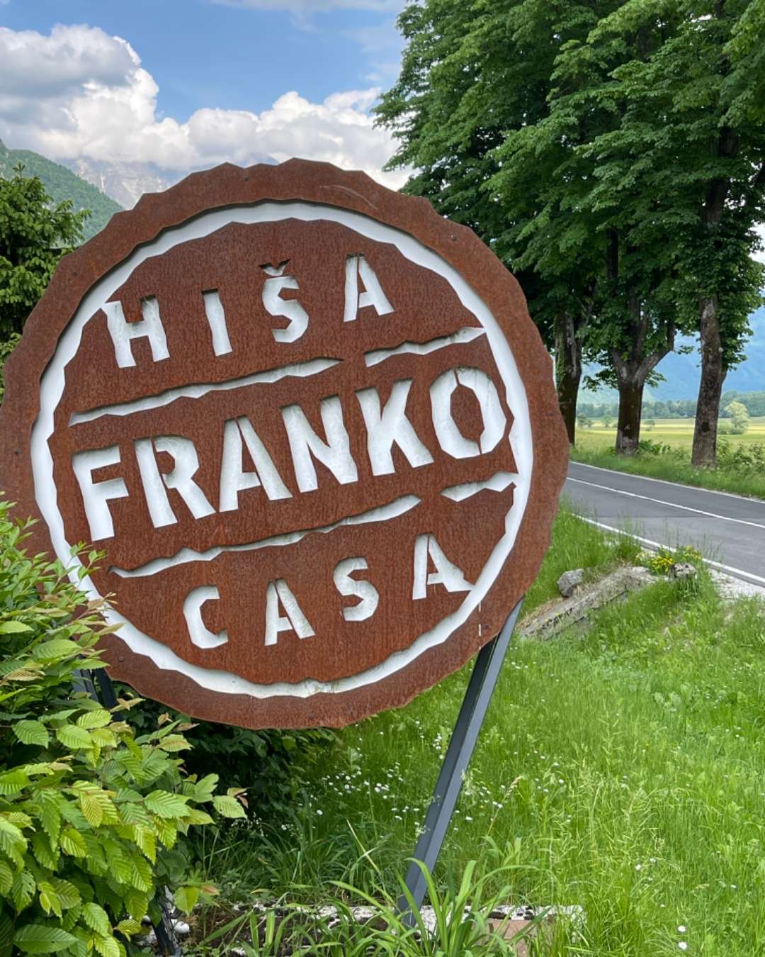 Brick color and white lettering sign for Hisa Franko in Slovenia with trees and grass behind